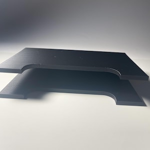 May include: Two black, rectangular wooden shelves with curved cutouts on the sides are stacked on top of each other. The shelves have a matte finish and are set against a white background.