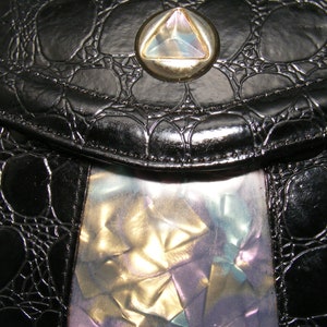 May include: A black leather purse with a textured crocodile pattern and a silver and iridescent triangle-shaped clasp.