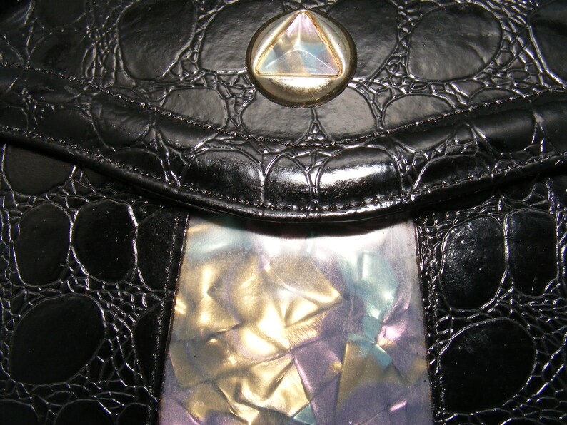 May include: A black leather purse with a textured crocodile pattern and a silver and iridescent triangle-shaped clasp.