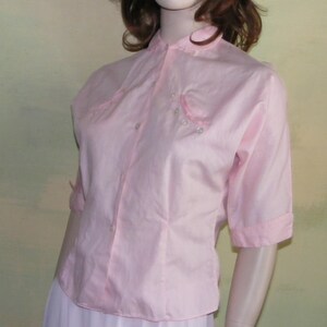 May include: A pink short-sleeved button-up blouse with a mandarin collar and pearl embellishments.