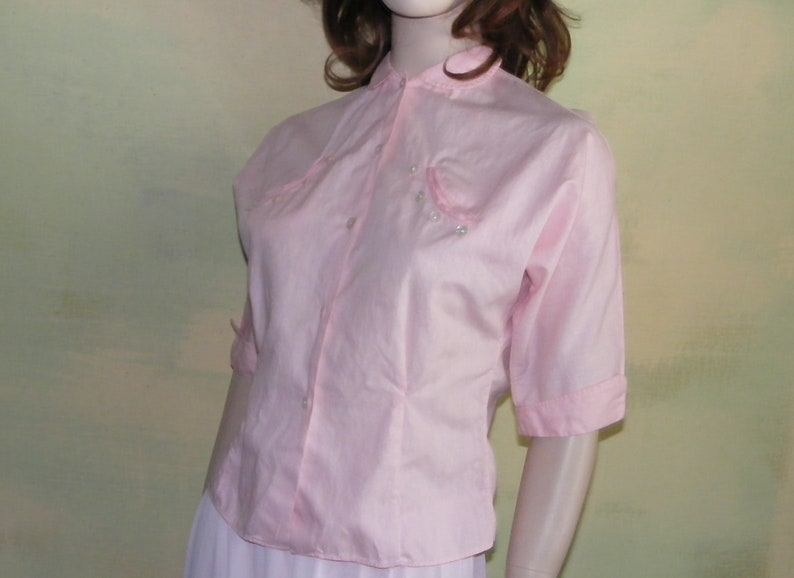 May include: A pink short-sleeved button-up blouse with a mandarin collar and pearl embellishments.
