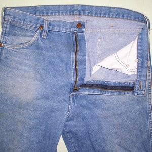 May include: A pair of blue denim jeans with a zipper fly and a button closure. The zipper is open and the fly is turned back to reveal the inside of the jeans.