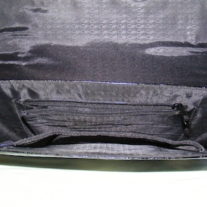 May include: Black patent leather purse with a zippered pocket and multiple compartments inside.