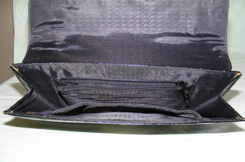 May include: Black patent leather purse with a zippered pocket and multiple compartments inside.