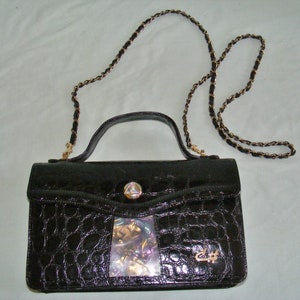 May include: A black crocodile-embossed leather handbag with a gold chain strap and a decorative gold clasp. The bag has a clear plastic insert with iridescent material inside.