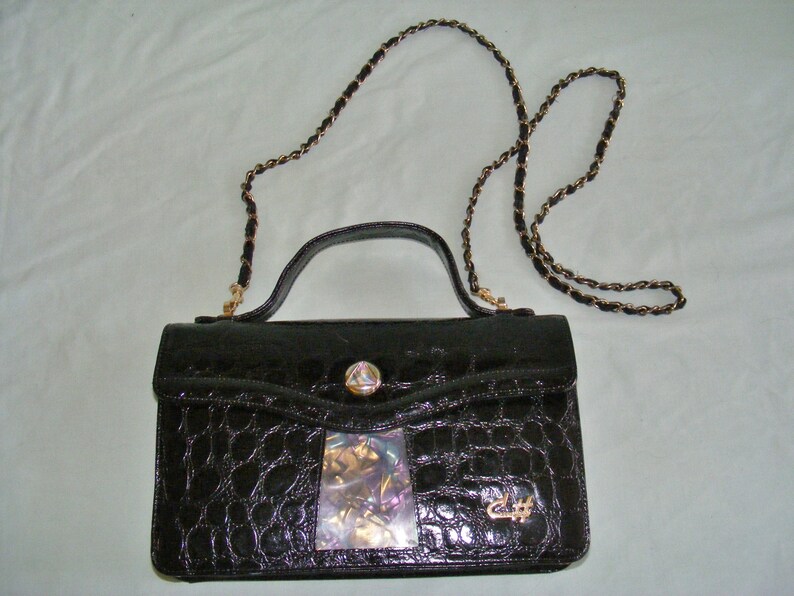 May include: A black crocodile-embossed leather handbag with a gold chain strap and a decorative gold clasp. The bag has a clear plastic insert with iridescent material inside.