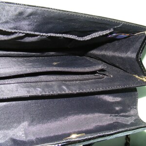 May include: Black leather purse with a zippered pocket inside. The purse has a gold chain strap.