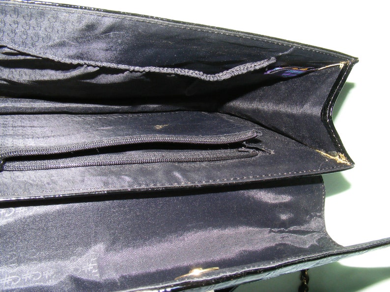 May include: Black leather purse with a zippered pocket inside. The purse has a gold chain strap.