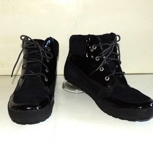 May include: A pair of black ankle boots with a lace-up closure. The boots have a shiny patent leather toe and a suede upper.
