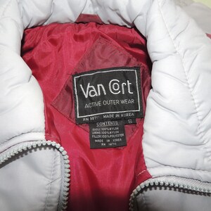 May include: A red and white puffer jacket with a black label that reads "Van @rt Active Outer Wear" and "RN 14711 MADE IN KOREA". The label also lists the contents as "SHELL: 100% NYLON, LINING: 100% NYLON, FILLER: 100% POLYESTER, MADE IN KOREA, RN 14711".