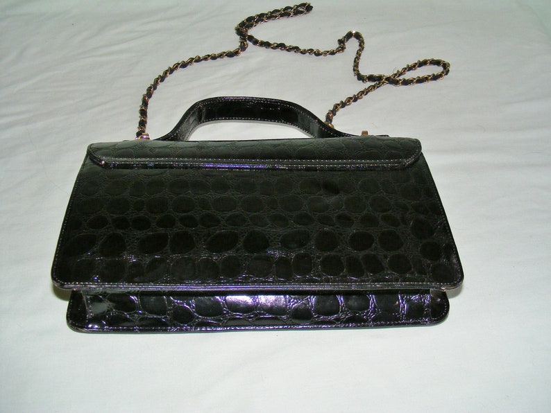 May include: A black crocodile embossed leather handbag with a gold chain strap.