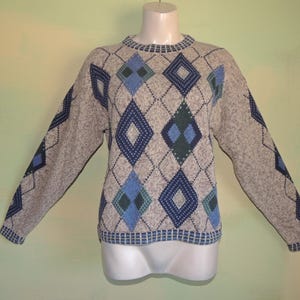 May include: A gray argyle sweater with blue and green diamond patterns. The sweater has long sleeves and a crew neck. The argyle pattern is repeated on the sleeves. The sweater is displayed on a mannequin.