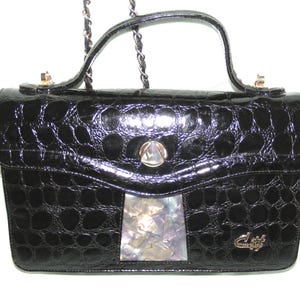 May include: A black crocodile-embossed leather handbag with a gold chain strap and a decorative shell inlay on the front.