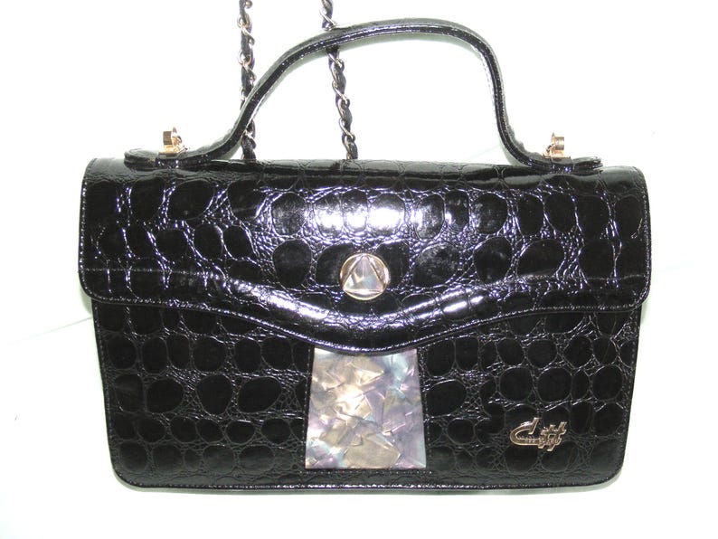 May include: A black crocodile-embossed leather handbag with a gold chain strap and a decorative shell inlay on the front.