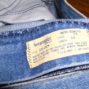 May include: A blue denim jean with a Wrangler brand label. The label states "Style 936 Den" and "Mens Slim Fit". The waist size is 36 inches and the length is 36 inches. The label also includes instructions for washing and drying the jeans.