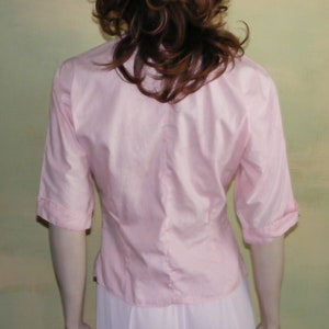 May include: A pink, short-sleeved button-down blouse with a fitted waist.
