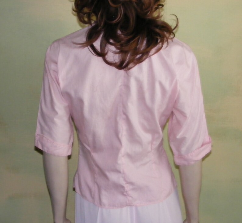 May include: A pink, short-sleeved button-down blouse with a fitted waist.