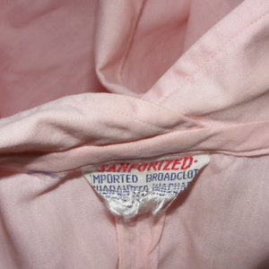 May include: A close-up of a pink fabric label with the text "Sanforized. Imported Broadcloth" in blue.