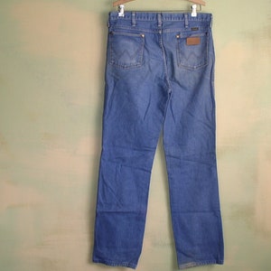May include: A pair of blue denim jeans with a brown leather patch on the back pocket. The jeans have a straight leg and a classic fit.