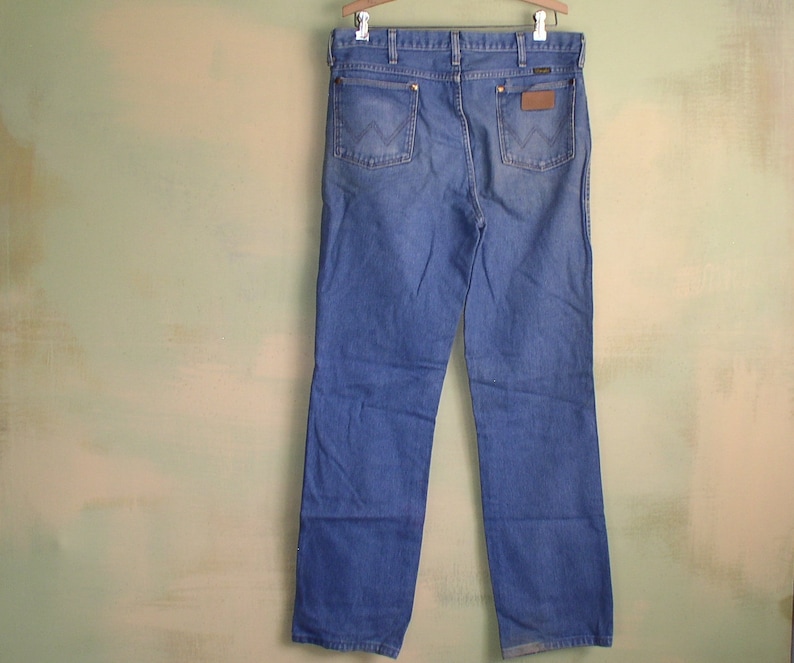 May include: A pair of blue denim jeans with a brown leather patch on the back pocket. The jeans have a straight leg and a classic fit.