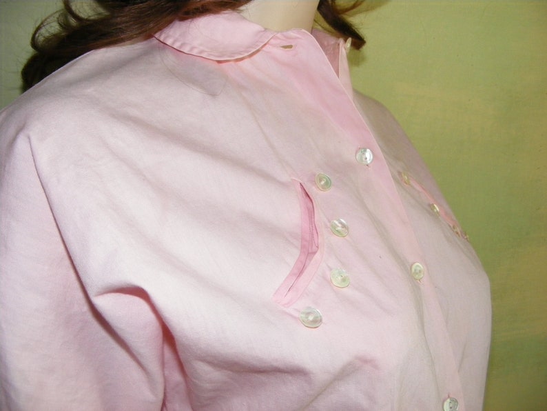 May include: A pink button-down shirt with a collar and a pocket on the left side. The shirt has pearl-like buttons.