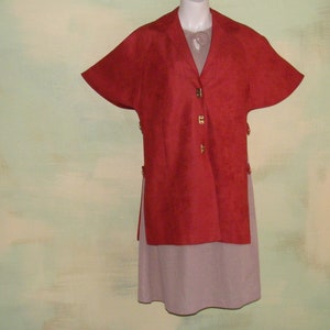 May include: A red suede jacket with short sleeves and gold buttons. The jacket is worn over a light purple dress.