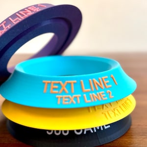Può includere: Una pila di oggetti circolari colorati con testo. L'oggetto superiore è viola con la scritta "TEXT LINE 1". Sotto c'è un oggetto turchese con "TEXT LINE 1" e "TEXT LINE 2". L'oggetto successivo è giallo e quello inferiore è nero.