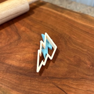 Può includere: Un tagliapasta a forma di fulmine in plastica bianca su una superficie di legno.