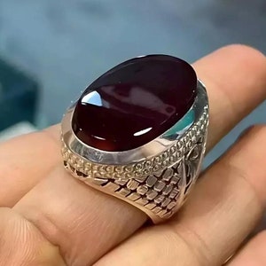 May include: A silver ring featuring a large, oval-shaped, dark red gemstone. The ring has intricate silver detailing around the stone and on the band.
