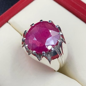 May include: A silver ring with a large, round, pink ruby gemstone set in a prong setting. The ring has a textured band.