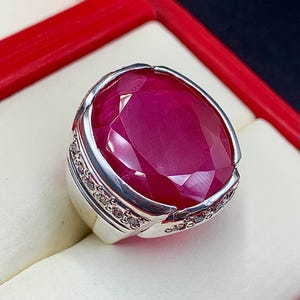 May include: A silver ring with a large, faceted, pink gemstone set in a bezel setting. The ring is surrounded by a band of smaller, clear gemstones.