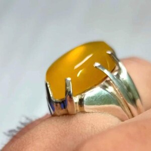 May include: A silver ring with a yellow oval gemstone set in a prong setting. The ring has a decorative band with a blue accent.