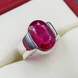 May include: A silver ring with a large, oval-shaped, bright red gemstone.
