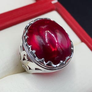 May include: A silver ring with a large, oval-shaped, deep red gemstone set in a decorative, ornate setting.