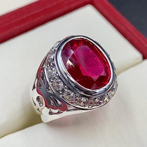 May include: A silver ring with a large oval-shaped red gemstone surrounded by smaller white gemstones.