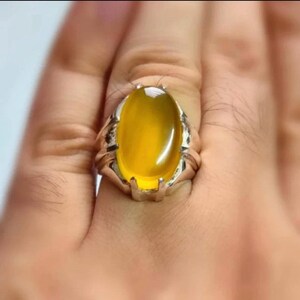 May include: A silver ring with a large, oval-shaped yellow gemstone set in the center. The ring has a detailed, ornate design.