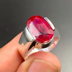 May include: A silver ring with a large, oval-shaped, red gemstone.
