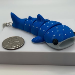 May include: A blue and white whale shark keychain with white spots. The keychain is made of plastic and has a silver metal ring.