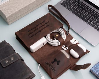 May include: A dark brown leather tech organizer roll featuring a wrist strap, internal pockets, and elastic loops holding white charging cables, a power adapter, and wireless earbuds. The leather is engraved with the text: You already have my heart, but here's a little something extra to make your day even sweeter!