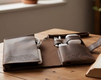 May include: Open brown leather tech organiser with multiple compartments. Contains a white phone, charging cables, and white wireless earbuds. The organiser has a wrist strap and the name "Christian" is embossed on the front.