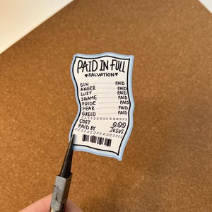 May include: A sticker in the shape of a receipt with the words "PAID IN FULL" and "SALVATION" at the top. The receipt lists "SIN, ANGER, LUST, SHAME, PRIDE, FEAR, GREED" with "PAID" next to each. The cost is listed as "0.00" and "PAID BY JESUS".