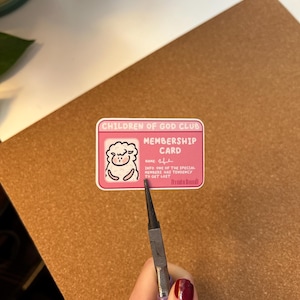 May include: A pink membership card for the "Children of God Club" featuring a sheep graphic. The card's text reads: "INFO: ONE OF THE SPECIAL MEMBERS HAS TENDENCY TO GET LOST."