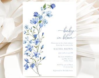 Puede incluir: Una invitación a una baby shower con una ilustración de acuarela de flores azules. El texto dice "baby in bloom" e incluye el nombre Rachel Brown, la fecha y hora de la ducha, la ubicación y la información de RSVP.