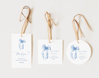 Può includere: Tre etichette regalo bianche con fiocchi acquerellati azzurri e cordini in pelle marrone. Un'etichetta dice "thank you" e "Lauren's Bridal Shower". Le altre due dicono "She's tying the knot" e "Lauren's Bridal Shower".