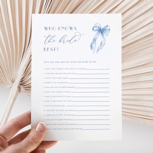 Puede incluir: Una tarjeta blanca con el texto "WHO KNOWS the bride BEST?" en escritura azul. Un gráfico de lazo de acuarela azul está en la esquina superior derecha. La tarjeta es un juego de despedida de soltera con preguntas para completar.
