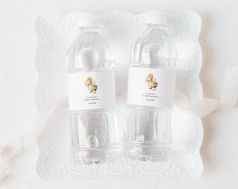 May include: Two clear plastic water bottles with white caps and labels. The labels feature a watercolor illustration of a duckling and the text "Lauren's Baby Shower" and a date. The bottles are on a white, decorative tray.