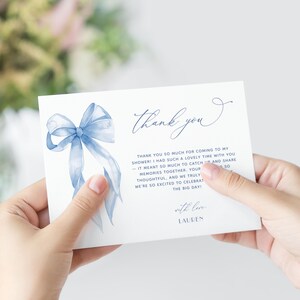 May include: A white card featuring a watercolour blue bow and the words "thank you" in elegant script. The card includes a thank you message and is signed "Lauren".