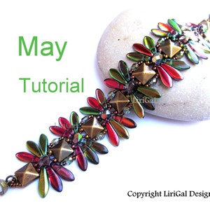 May include: A beaded bracelet with a geometric design in shades of red, green, and gold. The bracelet is made with seed beads and features a unique pattern of overlapping leaves. The bracelet is resting on a gray stone.