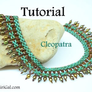 Op de afbeelding: Een turquoise en bruine kralenketting met een franje van parels. De ketting heet "Cleopatra" en wordt getoond op een rots. De tekst "Tutorial" staat bovenaan de afbeelding.