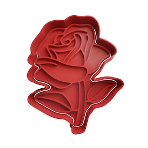 May include: A red rose-shaped cookie cutter with a stem and leaves. The cutter has a detailed design of the rose petals and is made of a flexible material. The white outline defines the shape of the rose.